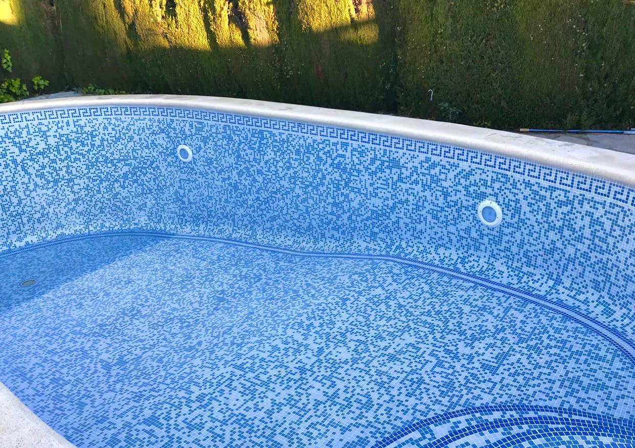 Sanierter Pool mit blauem Mosaikmuster und umliegender Hecke