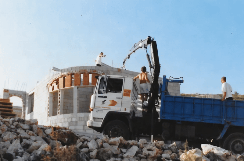 Bauarbeiter auf einer Baustelle mit LKW und Baggerarm – frühe Phase eines Bauprojekts von Immobilien Service Kryzon.